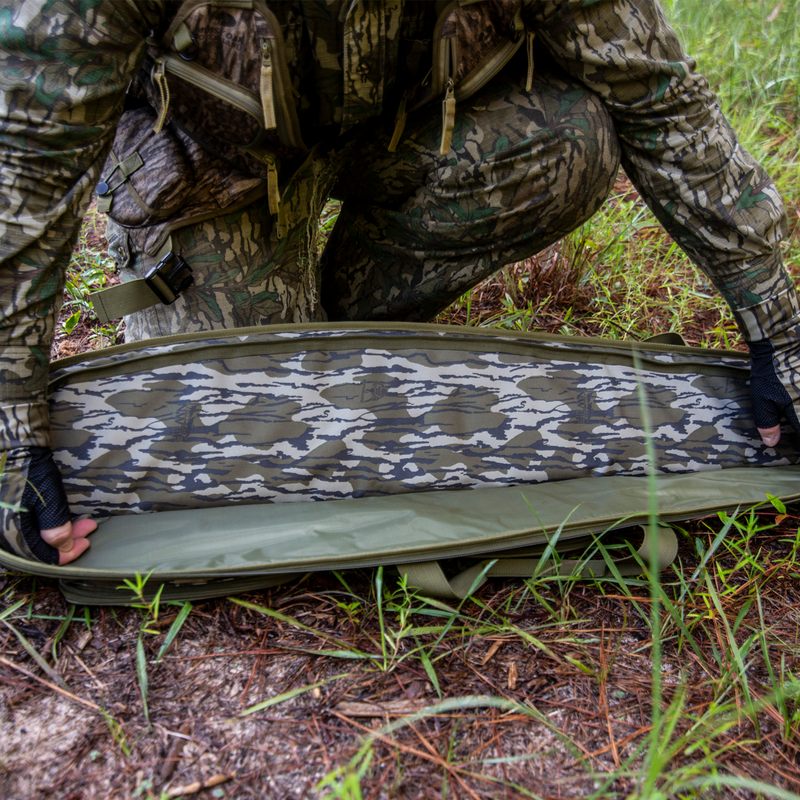 Load image into Gallery viewer, Person in Mossy Oak Bottomland opens a Primos Mossy Oak Bottomland Shotgun Case with choke tube holders on grass.
