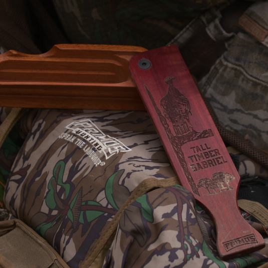 The Primos Tall Timber Gabriel Turkey Call sits on a camo backpack, ready for your next turkey hunt.