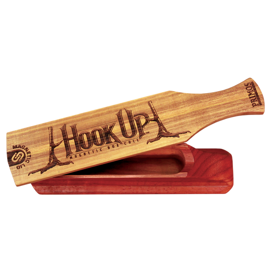 A Primos Hook Up Magnetic Turkey Call with a magnetic lid sits atop its labeled wooden base.