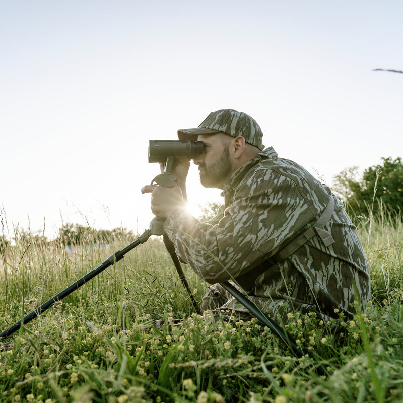 Load image into Gallery viewer, Person in camouflage gear using a metal detector in a grassy field.
