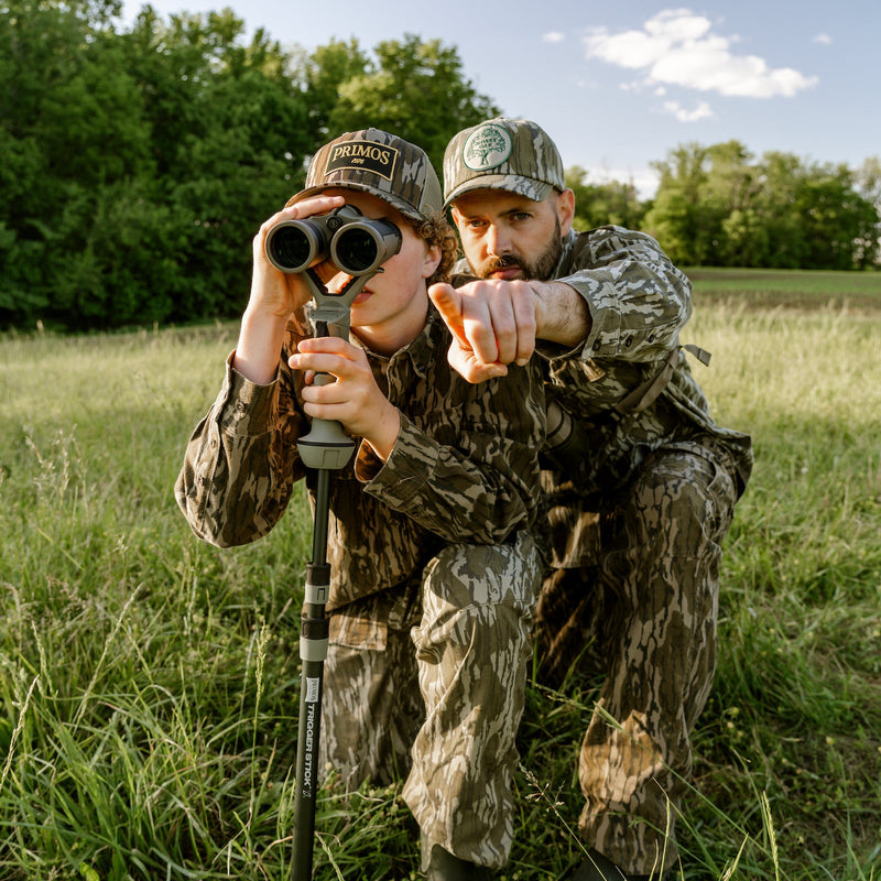Load image into Gallery viewer, Two hunters in camouflage gear in a field, one using binoculars.
