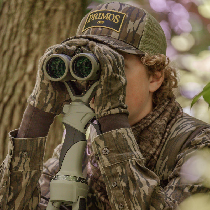 Load image into Gallery viewer, Person in full camouflage gear using binoculars with a Primos cap.
