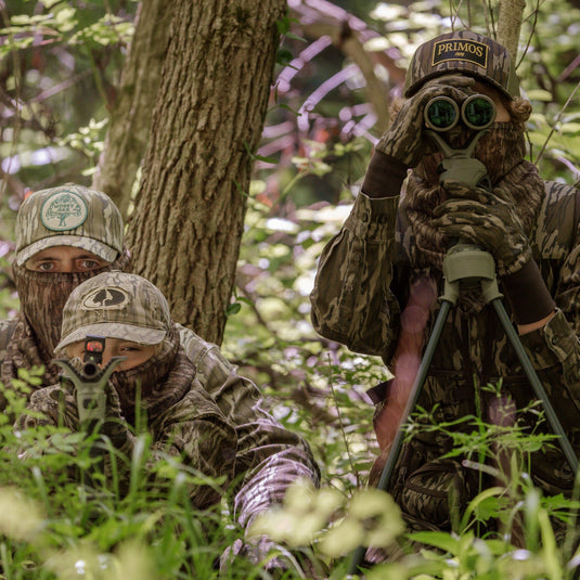 Two hunters in camouflage gear in a forest setting, one using binoculars.