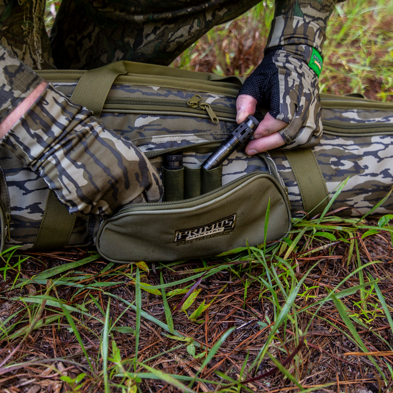 Load image into Gallery viewer, A person in camo puts choke tube holders in a green Realtree bag next to a Primos Mossy Oak Bottomland Shotgun Case.
