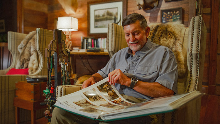 Smiling man sitting in an armchair, looking through a large photo album in a cozy, warmly lit room.