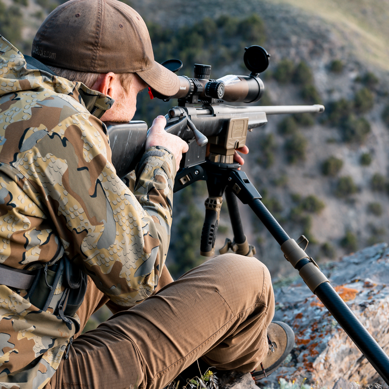 Load image into Gallery viewer, A person in camo kneels outdoors, aiming a rifle on the Primos Trigger Stick Apex Carbon Fiber Tripod.
