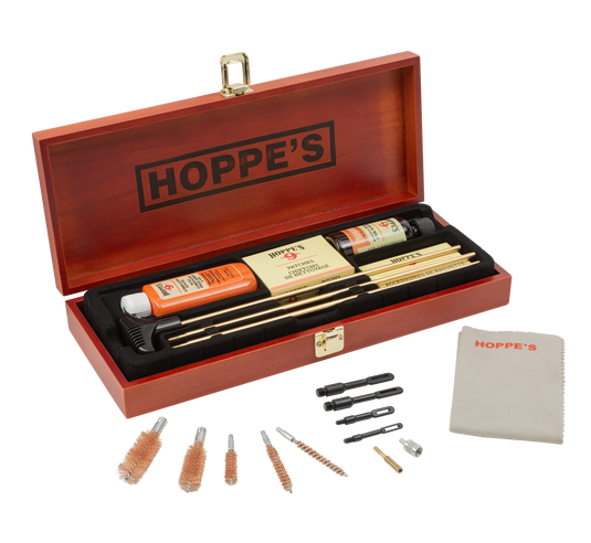 The Deluxe Gun Cleaning Kit comes in a wooden Hoppe's box and includes rods, brushes, Hoppe's No. 9 cleaning solution, a cloth, and multiple tool attachments—everything needed for complete firearm care arranged inside and in front of the box.