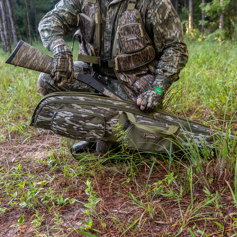 Load image into Gallery viewer, A person in Mossy Oak Bottomland holds a Primos Mossy Oak Bottomland Shotgun Case while kneeling in the woods.
