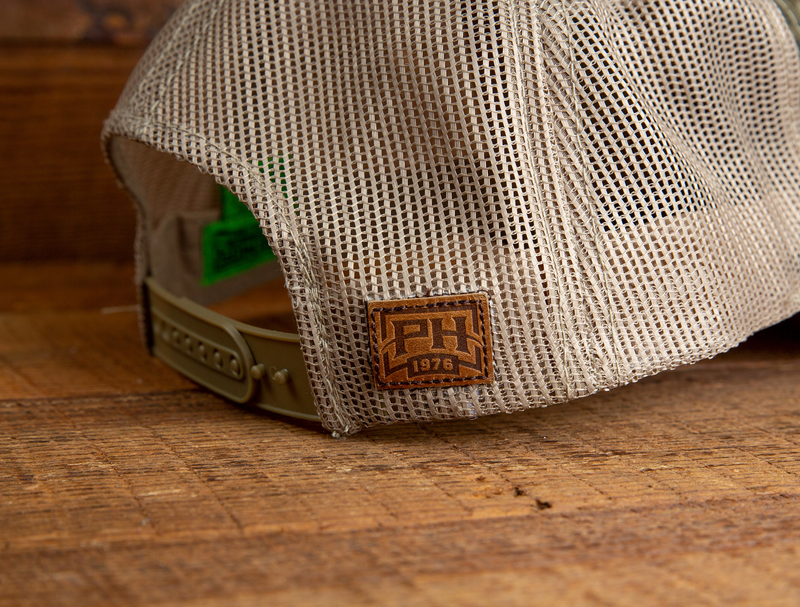 Load image into Gallery viewer, A Mossy Oak Original Bottomland Hat by Primos with mesh back and brown PH 1976 patch rests on a wooden surface.

