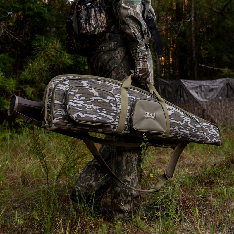Load image into Gallery viewer, Person in Primos camo carries a Mossy Oak Bottomland Scoped Rifle Case outdoors near tents and tall grass.
