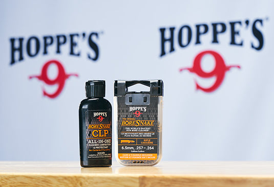 Two Hoppe’s 9 BoreSnake gun cleaning products on a wooden surface, with a blurred Hoppe’s 9 logo in the background.